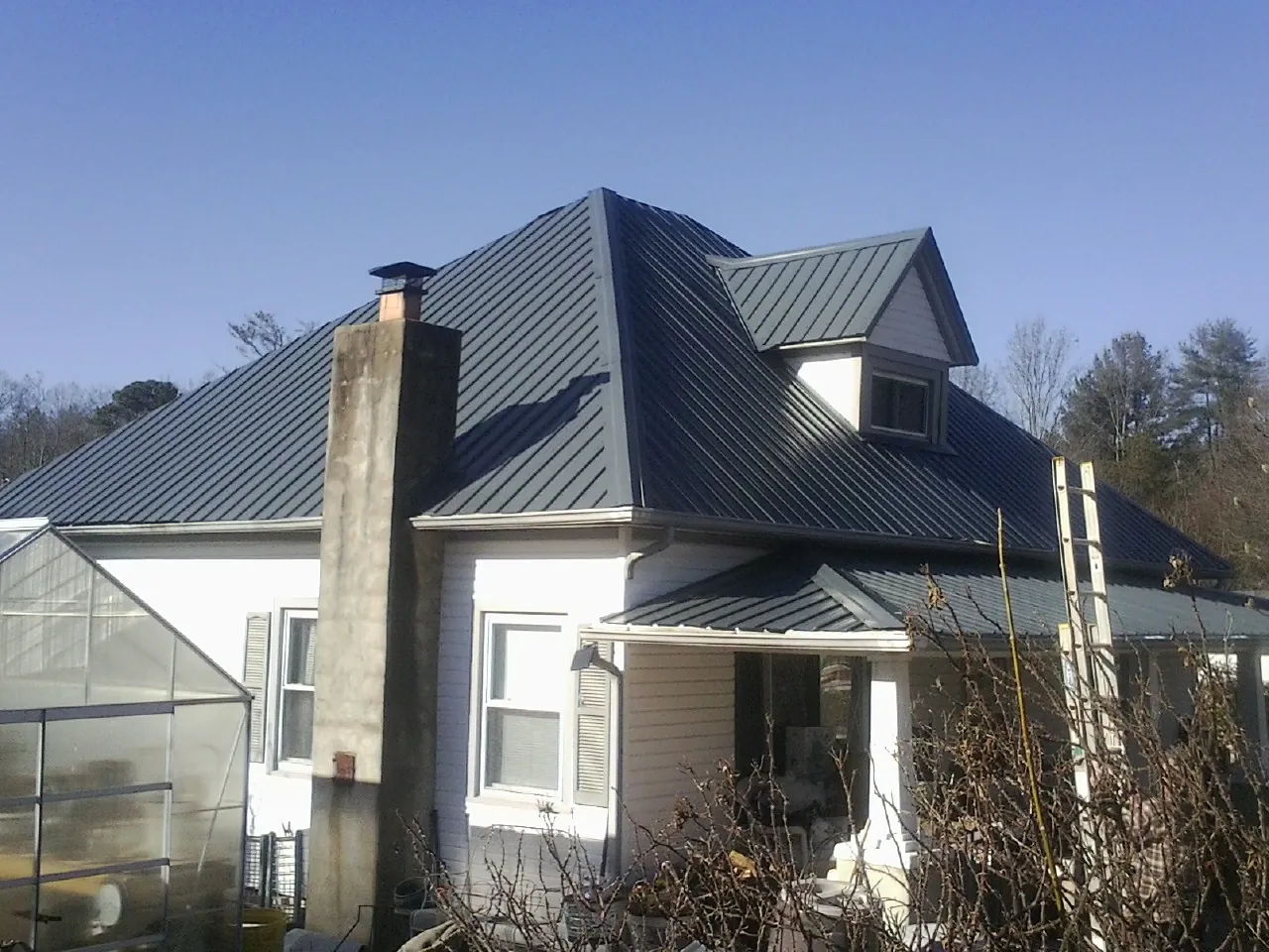 Dark blue standing seam metal roof on a white farmhouse with dormer — Slate & Tile Roof Repair by Roofing Brothers in Burr