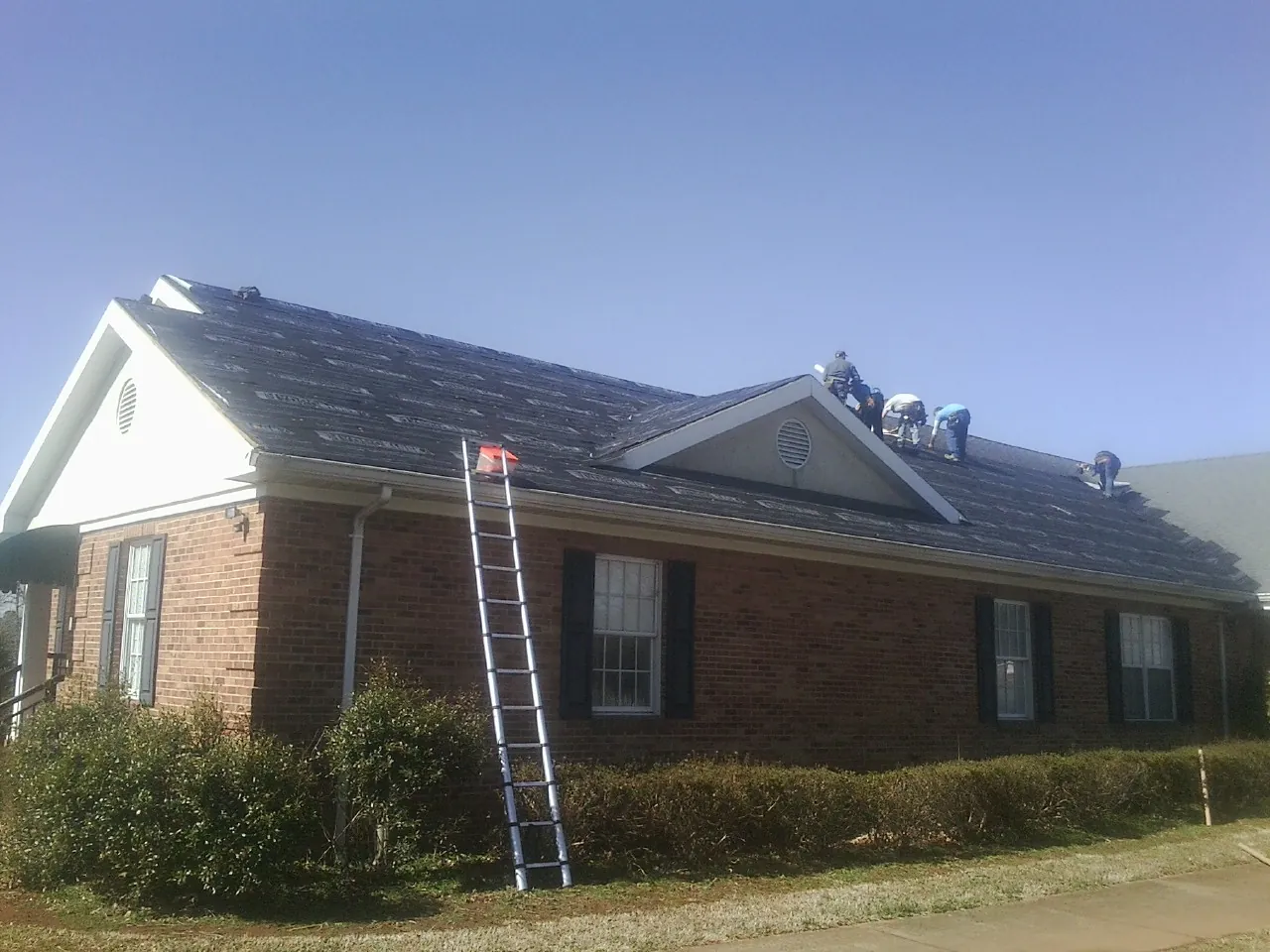 Crew tearing shingles off a brick ranch roof with a ladder set — Emergency Roof Repair work by our crew in Burr