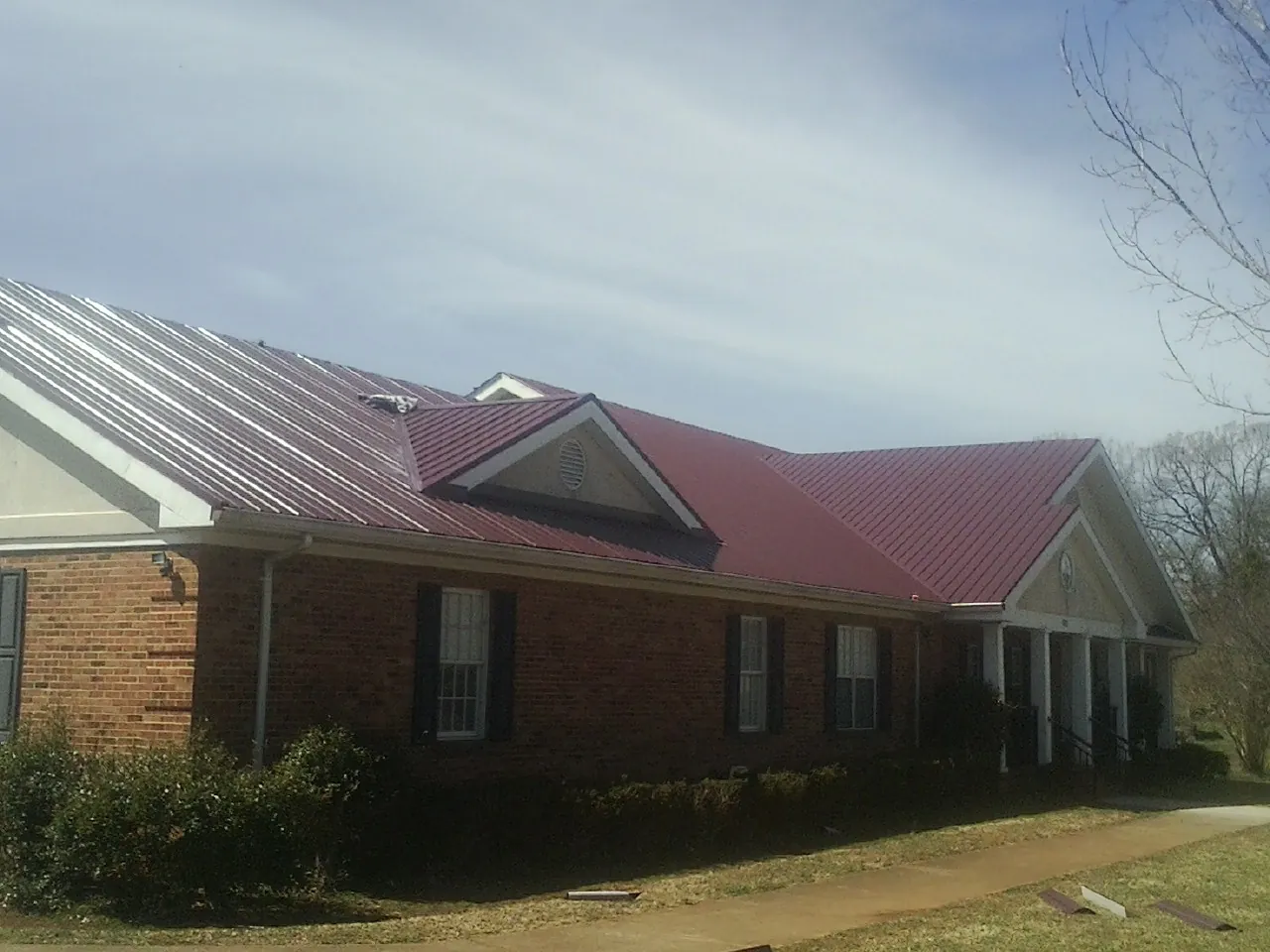 Red metal roof with gabled entries on a long brick building, from a Hail Damage Roof Repair job in Burr