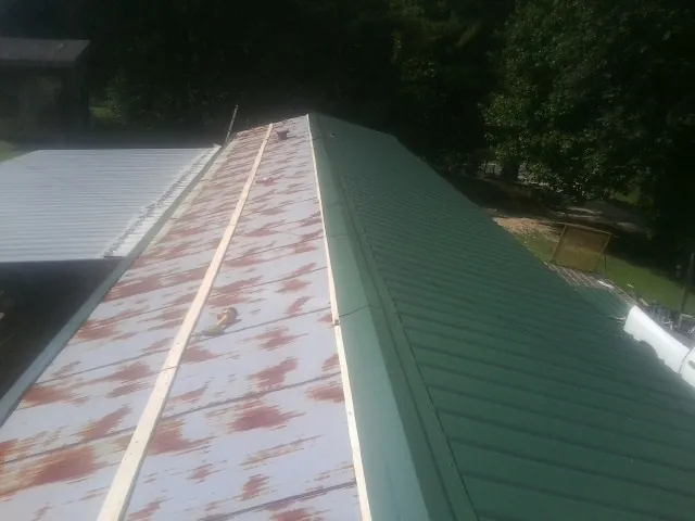 Old rusted panels beside newly installed green metal roofing — Wind Damage Roof Repair by Roofing Brothers in Burr