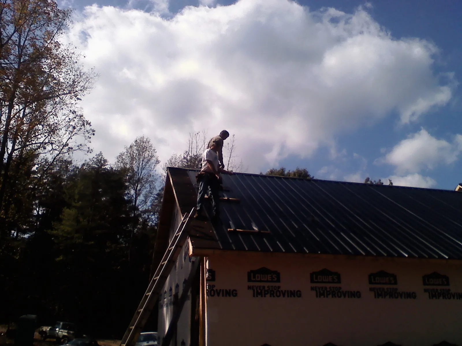 Roofer fastening dark metal panels high against a cloudy sky, from a Roof Inspection job in Burr