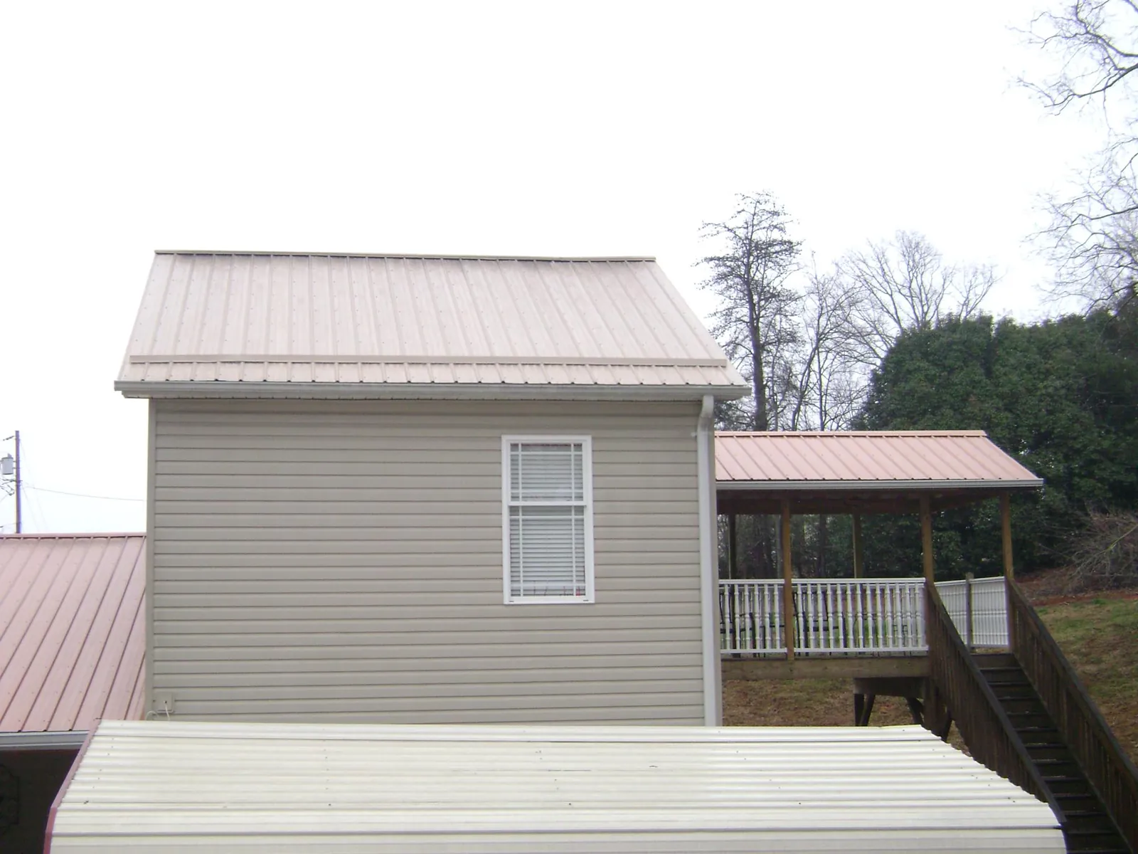 Tan metal roofs on a two story addition and attached porch, from a Roof Replacement job in Burr